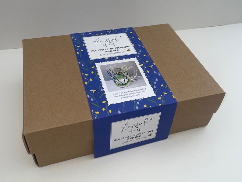 May include: A brown cardboard box with a blue and yellow label. The label says "glassful of art" and "Bluebells, Buttercups and Bee Glass Painting Kit". The box contains a glass painting kit.