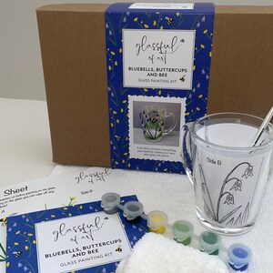 May include: A glass painting kit featuring a clear glass mug with a bluebell, buttercup, and bee design. The kit includes paints, brushes, and a practice sheet. The box is blue with a floral pattern and the text "glassful of art BLUEBELLS, BUTTERCUPS AND BEE GLASS PAINTING KIT".