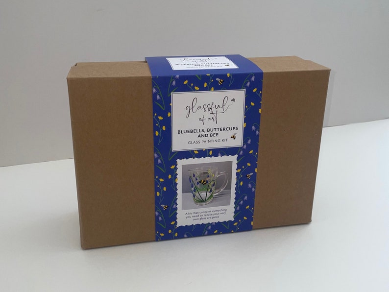 May include: A brown cardboard box with a blue and yellow label. The label says "glassful of art" and "Bluebells, Buttercups and Bee Glass Painting Kit". The label also shows a glass mug with a painted design of bluebells, buttercups, and a bee.