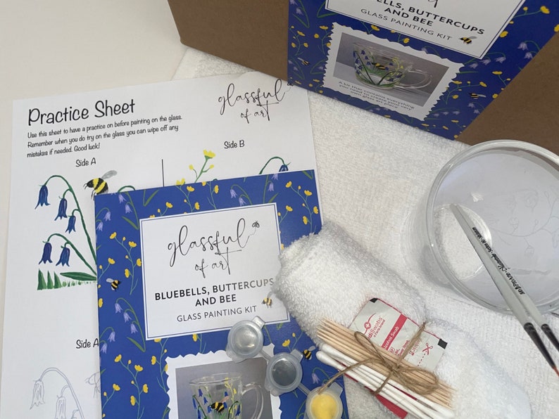 May include: A glass painting kit with a blue, yellow, and white design featuring bluebells, buttercups, and bees. The kit includes a glass mug, paint, brushes, and instructions. The kit is labeled "glassful of art" and "Bluebells, Buttercups and Bee Glass Painting Kit".