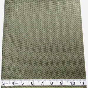 Puede incluir: Una pieza de tela verde doblada con un patrón repetitivo de estilo tejido en verde oscuro y beige, con pequeños puntos rojos. Una cinta métrica blanca es visible en la parte inferior, mostrando un ancho de unos 20 cm. El texto dice SUGAR HOUSE.