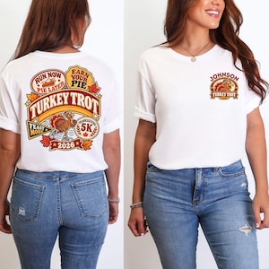 May include: A white t-shirt featuring a graphic print. The back displays a turkey running with text reading RUN NOW PIE LATER, EARN YOUR PIE, TURKEY TROT, FEAST MODE, THANKSGIVING 5K, and 2026. The front chest features a smaller turkey graphic with JOHNSON TURKEY TROT 2026.