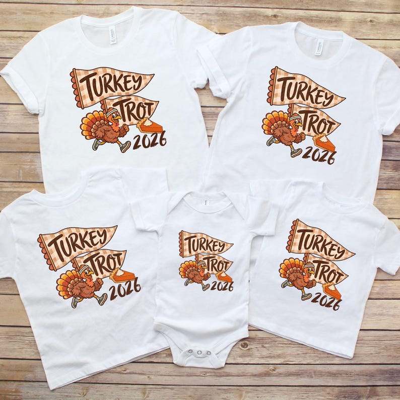 May include: A collection of white t-shirts and a white baby bodysuit featuring a graphic of a running turkey wearing a headband, a checkered pennant flag with the text Turkey Trot, a slice of pumpkin pie, and the year 2026 in brown lettering.