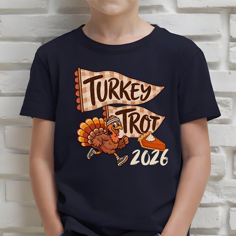 May include: A dark navy blue t-shirt featuring a graphic of a running turkey wearing a headband and sneakers. Above the turkey are two beige checkered pennants with the text "TURKEY TROT" and a slice of pumpkin pie next to the year "2026".