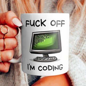 Könnte beinhalten: Weiße Keramik-Tasse mit dem Text "FUCK OFF I'M CODING" und einer Grafik eines Computermonitors mit grünem Code. Die Tasse hat einen Standardgriff und eine glänzende Oberfläche.