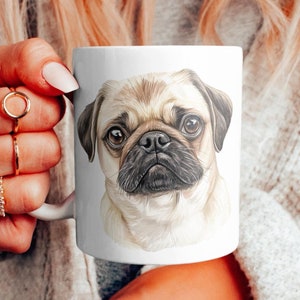 K&ouml;nnte beinhalten: Wei&szlig;e Keramiktasse mit einer Aquarell-Illustration eines Mopsgesichts. Der Mops hat ein hellbraunes und wei&szlig;es Fell.