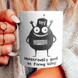 Może przedstawiać: Biały kubek ceramiczny z czarno-białym rysunkiem potwora w czapce "nerd". Potwór trzyma klawiaturę, a pod rysunkiem widnieje napis "Monstrously good at fixing you!"