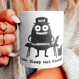 Op de afbeelding: Een witte keramische mok met een zwart-witte illustratie van een monster dat een hoed draagt met de tekst "nerd". Het monster zit aan een bureau met een laptop en een kop koffie. De tekst op de mok luidt "404: Sleep Not Found!"