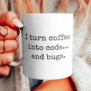Op de afbeelding: Een witte koffiemok met zwarte tekst die "Ik verander koffie in code... en bugs." zegt.