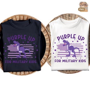 Pode incluir: Duas camisetas com um gráfico de dinossauro roxo e o texto "Purple Up for Military Kids". As camisetas são azul marinho e brancas.