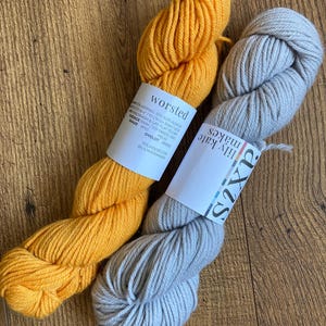May include: Two skeins of yarn, one yellow and one grey, with labels that read "worsted" and "axis makes lily, kate".