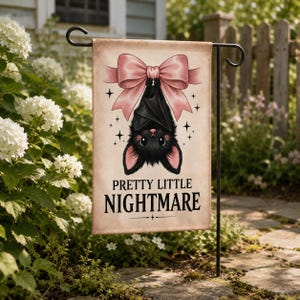 May include: A rectangular garden flag featuring a black bat hanging upside down from a large, light pink bow. The background is a light beige color with small black star accents. The text "PRETTY LITTLE NIGHTMARE" is printed in black below the bat.