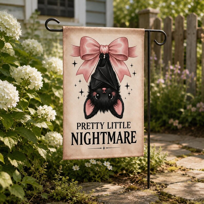 May include: A rectangular garden flag featuring a black bat hanging upside down from a large, light pink bow. The background is a light beige color with small black star accents. The text "PRETTY LITTLE NIGHTMARE" is printed in black below the bat.