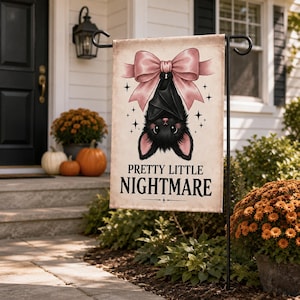 May include: A rectangular garden flag featuring a black bat hanging upside down from a large pink bow. The bat has pink inner ears and nose. The text PRETTY LITTLE NIGHTMARE is printed in black below the bat, surrounded by small star icons.