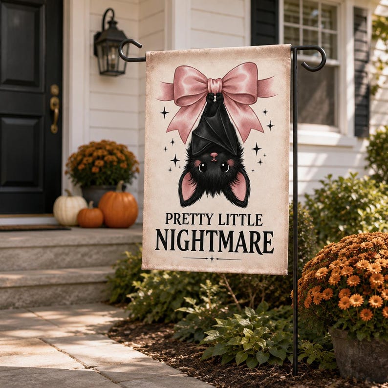 May include: A rectangular garden flag featuring a black bat hanging upside down from a large pink bow. The bat has pink inner ears and nose. The text PRETTY LITTLE NIGHTMARE is printed in black below the bat, surrounded by small star icons.