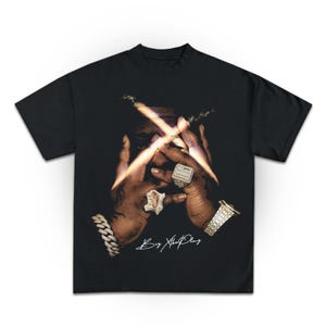 May include: Black t-shirt with a graphic of a person's face with their hands covering their eyes. The graphic is in black and white with a gold and white cross over the eyes. The text "Big Xtha Play" is written in white below the graphic.