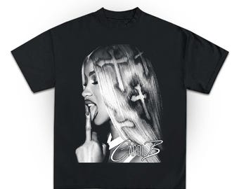 May include: Black t-shirt featuring a black and white graphic of a woman with long blonde hair, a finger to her lips, and her tongue out. The text "Cardi B" is printed in a stylized font below the image.