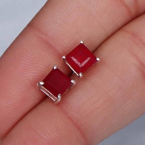 Può includere: Un paio di orecchini a perno d'argento con pietre preziose rosse quadrate.