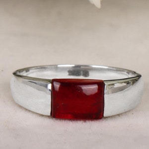 May include: A silver ring with a square red gemstone set in the center.