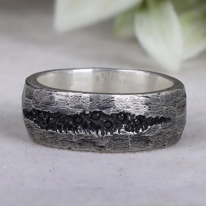 May include: A silver band ring with a textured finish and a row of black diamonds.