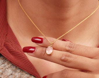 May include: A delicate gold chain necklace with a pink oval gemstone pendant.