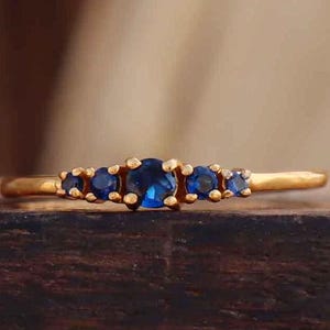 May include: A gold band ring with five small blue gemstones set in a curved line.
