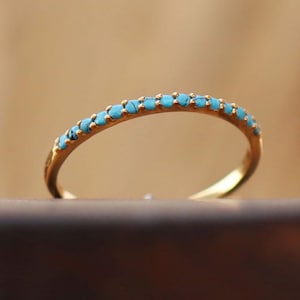 Può includere: Un delicato anello a fascia d'oro con una fila di pietre turchesi.