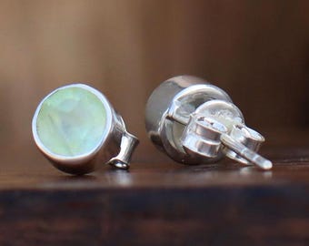 May include: A pair of silver stud earrings with a light green gemstone in the centre of each earring.