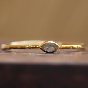 May include: A delicate gold ring with a marquise-shaped clear gemstone. The band is thin and has a hammered texture.