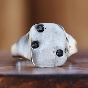 May include: A silver signet ring with a square face and three black gemstones.