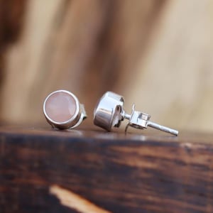 Può includere: Un paio di orecchini a perno d'argento con accenti di pietre preziose rosa. Gli orecchini sono mostrati su una superficie di legno.