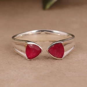May include: A silver ring with two red triangular gemstones set in the band.