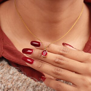 May include: A gold chain necklace with a red oval pendant. The pendant is set in a gold frame.