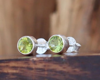 May include: A pair of silver stud earrings with round green peridot gemstones.