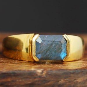 May include: A gold ring with a large, rectangular, blue labradorite gemstone set in a bezel setting.