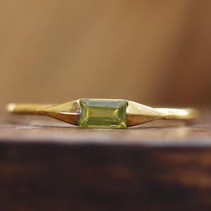 Puede incluir: Un anillo de oro con una piedra preciosa rectangular verde engastada en el centro.