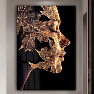 May include: An artistic wall print showing a woman's profile integrated with golden autumn leaves on a black backdrop. The leaves form a distinctive design, accentuating the facial features. A decorative piece for the home.