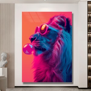 May include: A rectangular wall art print featuring a profile view of a lion wearing bright pink sunglasses and blowing a large pink bubblegum bubble. The lion is rendered in vibrant neon blue and purple tones against a solid orange background.