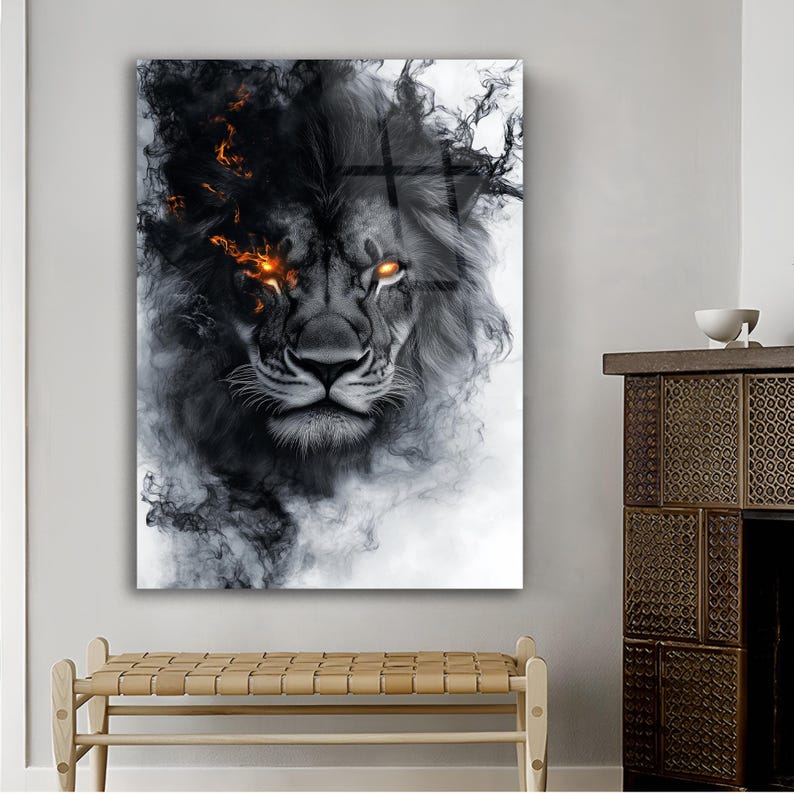 May include: A framed art print featuring a lion's face with a dark, smoky mane and fiery orange eyes. The artwork is predominantly black and white, with the lion's face centered and the smoke-like elements surrounding it. The print is displayed on a white wall.
