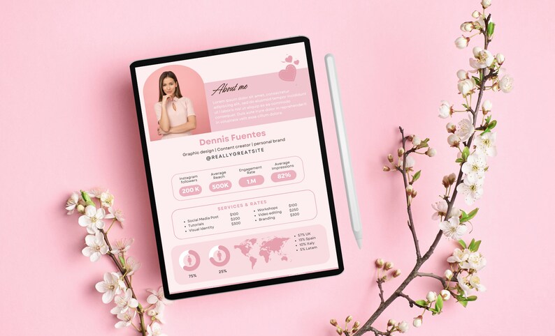 May include: A pink tablet screen displaying a resume for Dennis Fuentes, a graphic designer and content creator. The resume includes a headshot, social media statistics, services offered, and rates. The tablet is on a pink surface with a white stylus and a branch of white blossoms.