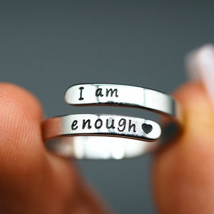 May include: Silver ring with the words "I am enough" and a small heart engraved on the band.