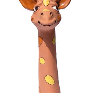 Könnte beinhalten: Keramik-Giraffenfigur mit langem Hals und lächelndem Gesicht. Die Giraffe hat braune und gelbe Flecken, große Ohren und kleine schwarze Hörner. Die Figur ist in Braun-, Gelb- und Schwarztönen bemalt.