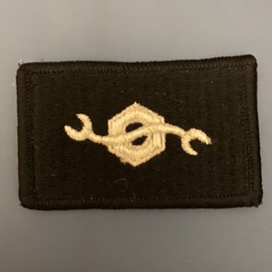 May include: A black rectangular patch with a white embroidered wrench and nut design.