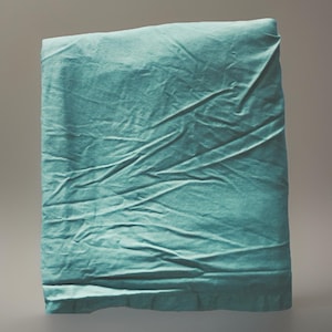 May include: A folded, teal-colored fabric with visible creases and folds. The fabric appears to be a sheet or blanket, with a soft, textured appearance. The teal color is consistent throughout the fabric, creating a calming aesthetic.