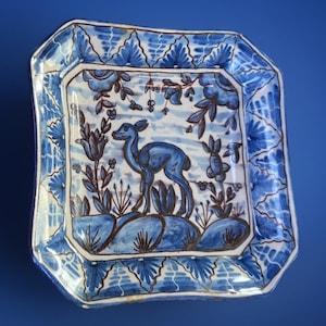 May include: Square ceramic plate with a blue and white floral and deer design. The plate features a central image of a deer surrounded by stylized plants and flowers. The border has a repeating floral pattern.