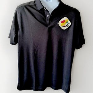 May include: A black short-sleeved polo shirt with a yellow, red, and green embroidered patch on the left chest.