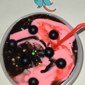 May include: A close-up of a clear plastic container filled with pink and brown slime. The slime is decorated with black beads and a red straw is sticking out of the top.