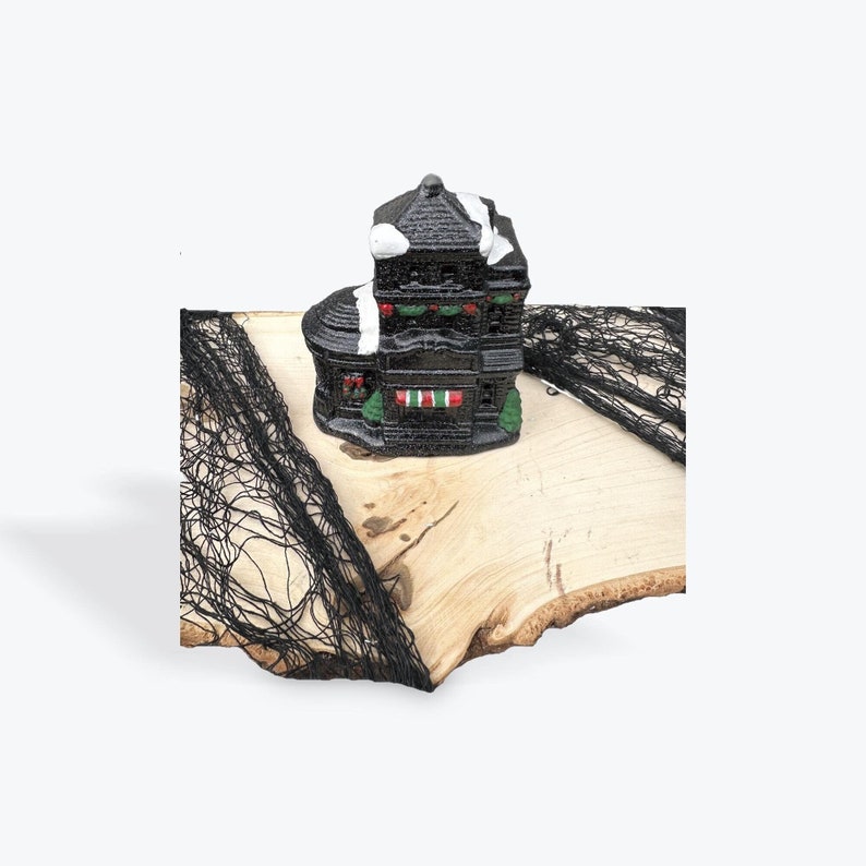 May include: Black and white ceramic house figurine with green accents, sitting on a wooden surface with black netting.