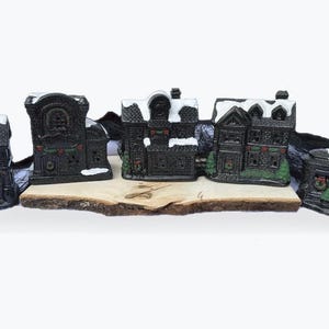 May include: Set of six black and white miniature houses with snow-covered roofs and green accents. The houses are arranged on a wooden base and are perfect for a Christmas village display.
