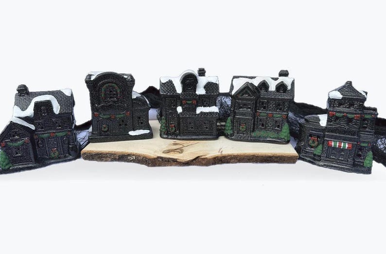 May include: Set of six black and white miniature houses with snow-covered roofs and green accents. The houses are arranged on a wooden base and are perfect for a Christmas village display.